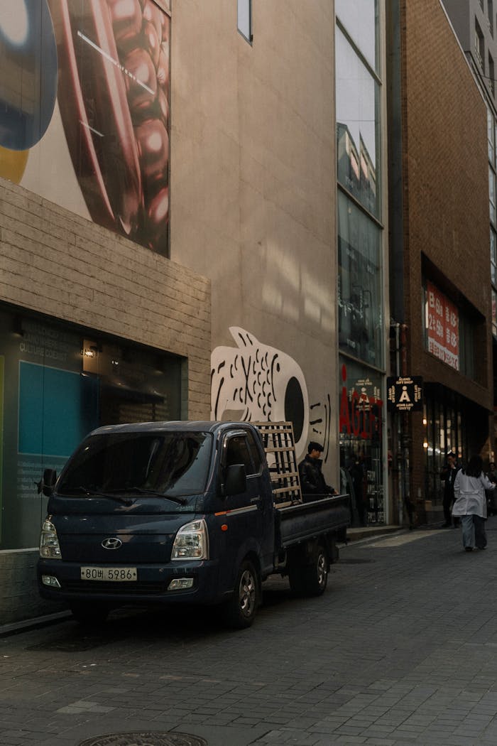 City street scene featuring a truck, pedestrians, and modern architecture.
